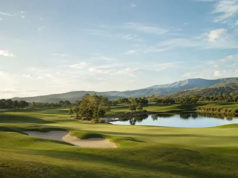 Uitgestrekte golfbaan met green, waterpartij, zandbunkers en bergen op de achtergrond